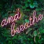 And breathe” neon sign symbolizing a mindful pause and simple stress relief in everyday wellness