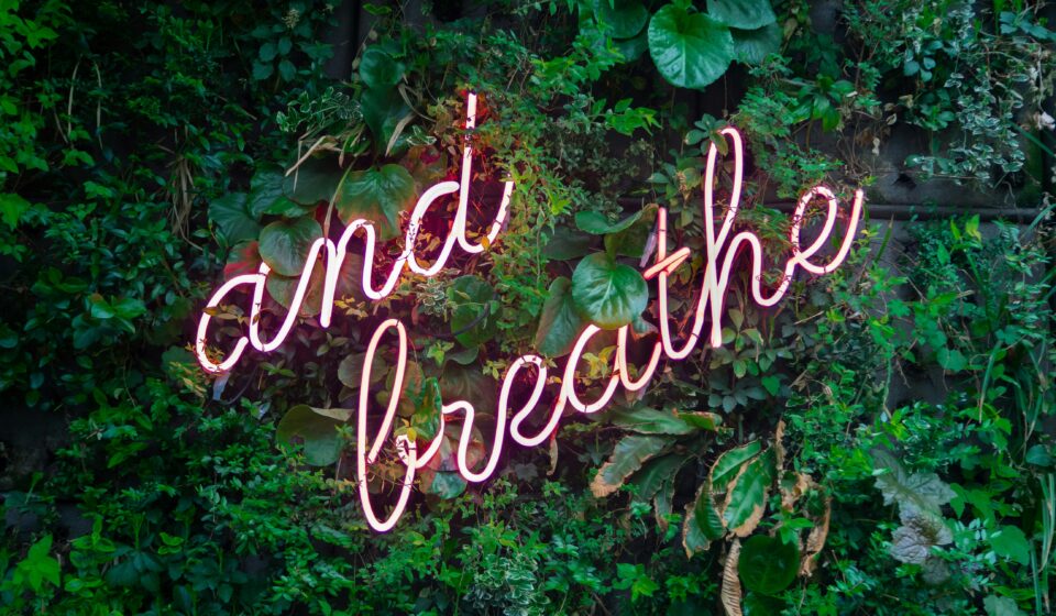 And breathe” neon sign symbolizing a mindful pause and simple stress relief in everyday wellness