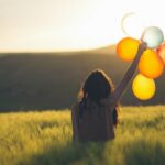 Person holding a bundle of colorful balloons outdoors in natural light