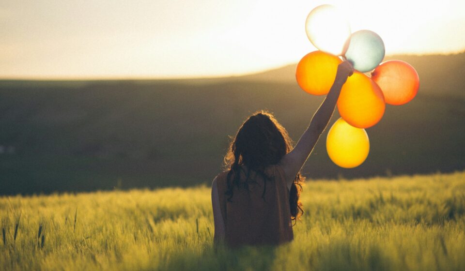 Person holding a bundle of colorful balloons outdoors in natural light