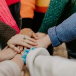 Group of people standing in a circle with their hands touching, representing shared connection and community