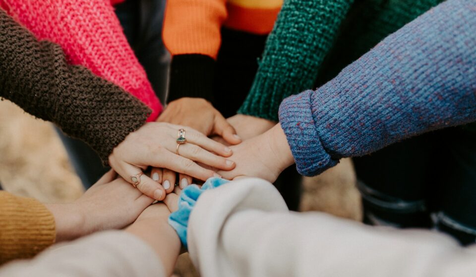 Group of people standing in a circle with their hands touching, representing shared connection and community