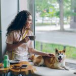 Woman sitting on a window sill next to her dog, taking a calm and quiet moment at home in natural light.