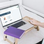 Person using a laptop while sitting on a bed in a calm home setting