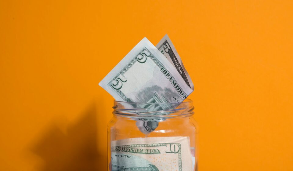Glass jar filled with coins and cash sitting on a table, representing simple savings habits