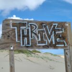 Wooden sign on a quiet beach with the word thrive written on it