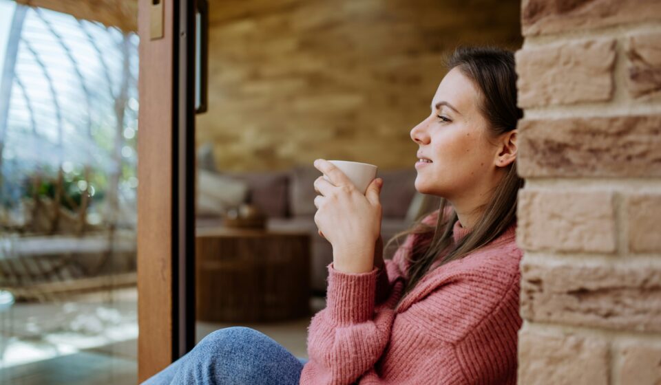 A busy woman enjoying a calm morning coffee at home, reflecting simple and realistic wellness through everyday self-care.