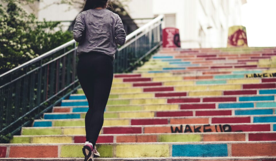 Woman jogging up outdoor stairs during a walk, showing simple everyday movement as part of realistic self-care.
