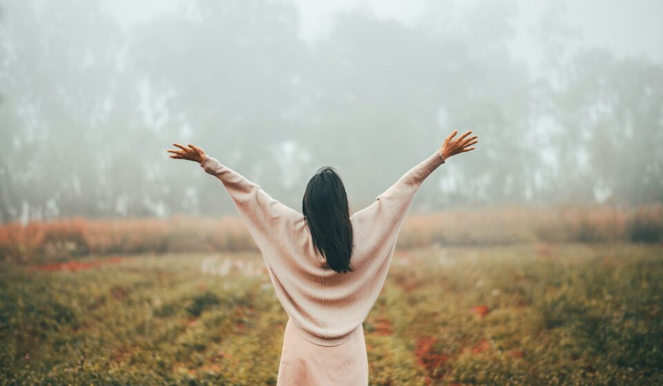Woman standing outdoors with arms open, taking a calm moment in a quiet natural setting