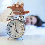 Woman lying in bed turning off an alarm clock in the morning