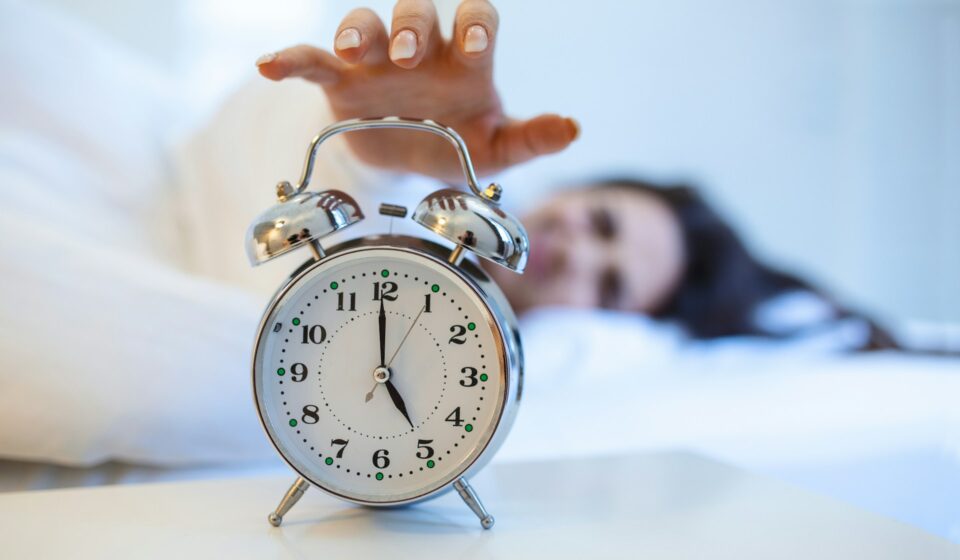 Woman lying in bed turning off an alarm clock in the morning