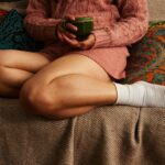 Woman sitting on a couch holding a cup, resting comfortably at home.
