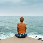 Woman sitting on a rock by the sea, looking out over the water on a quiet day.