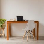 A quiet desk with a laptop and a small plant near a window, lit by soft natural light.