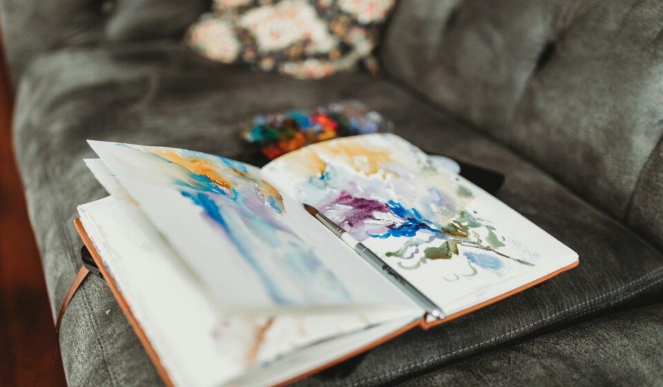 Watercolor journal and paintbrush resting on a couch