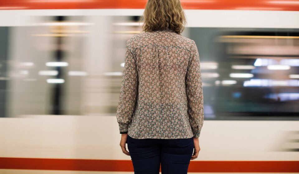 Rear view of a woman standing on a train platform as a train moves past
