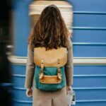Woman standing on a subway platform with a backpack as a train approaches