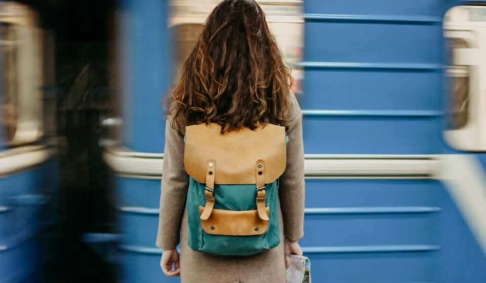 Woman standing on a subway platform with a backpack as a train approaches