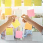 Person writing ideas on sticky notes on a glass board to organize tasks