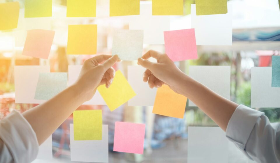 Person writing ideas on sticky notes on a glass board to organize tasks