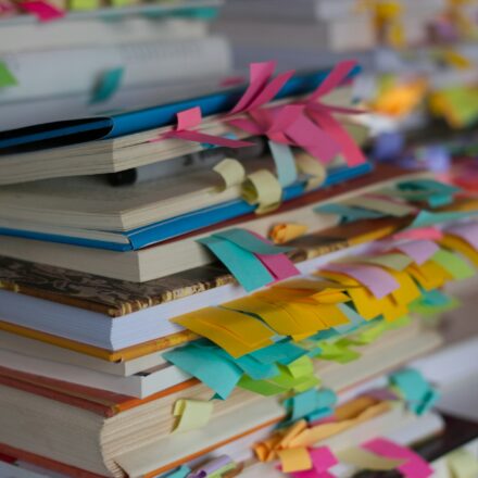 Stack of books with colorful bookmarks and ribbons showing multiple sections being tracked at once