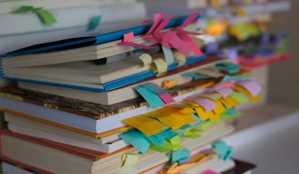 Stack of books with colorful bookmarks and ribbons showing multiple sections being tracked at once