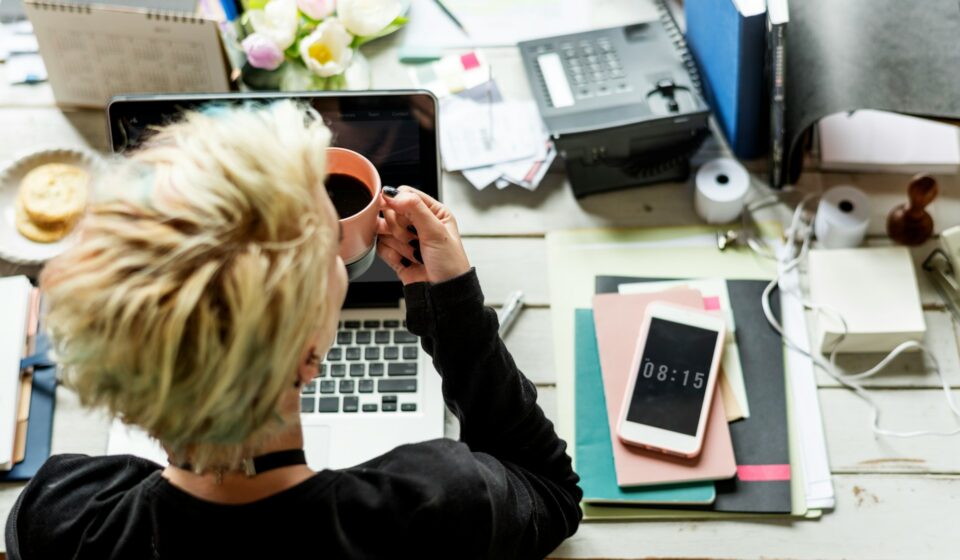 Hands holding a coffee cup beside a laptop during a quiet work moment at a desk