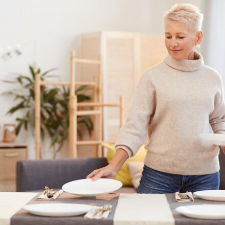 Woman placing a plate on the table while preparing for a family meal at home