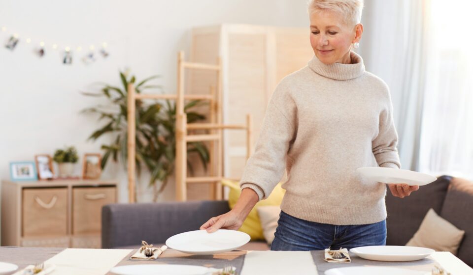 Woman placing a plate on the table while preparing for a family meal at home
