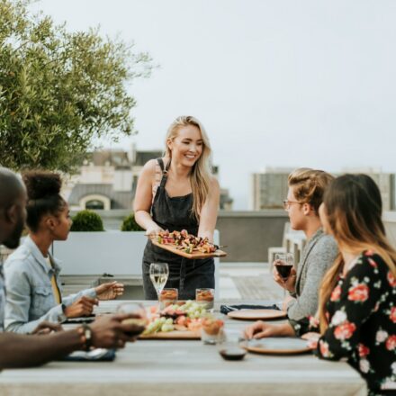 Woman serving food to friends gathered around an outdoor table