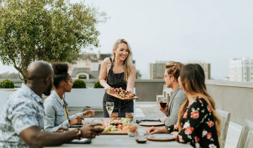 Woman serving food to friends gathered around an outdoor table