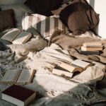 Cozy bed covered with blankets and cushions, with several open books scattered across the quilted bedspread.