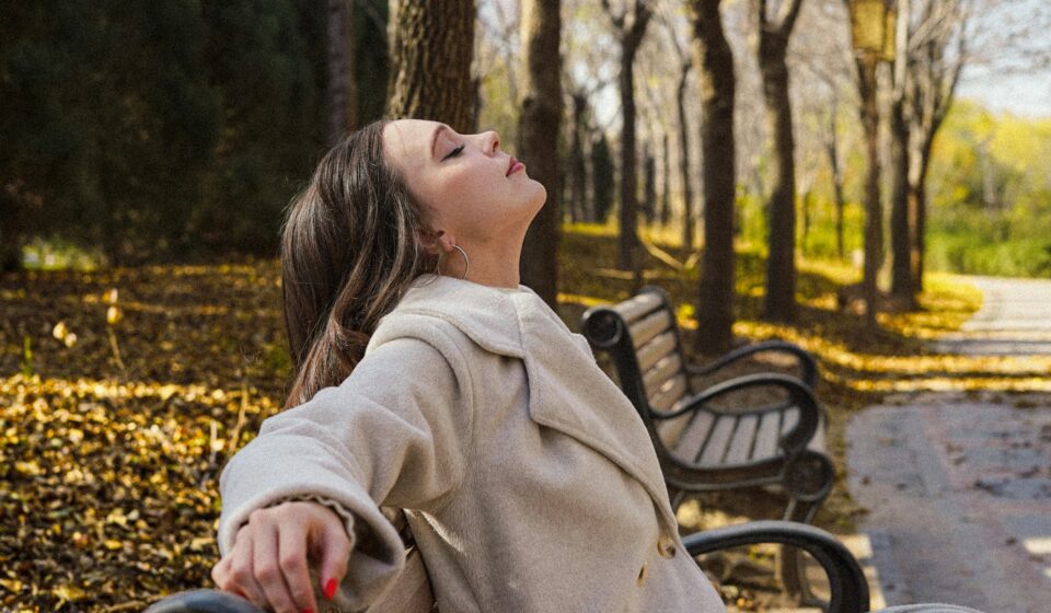 Woman relaxing on a park bench surrounded by autumn trees during a quiet moment outdoors