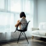 Woman sitting in a chair by a large window, quietly reflecting during a calm moment at home