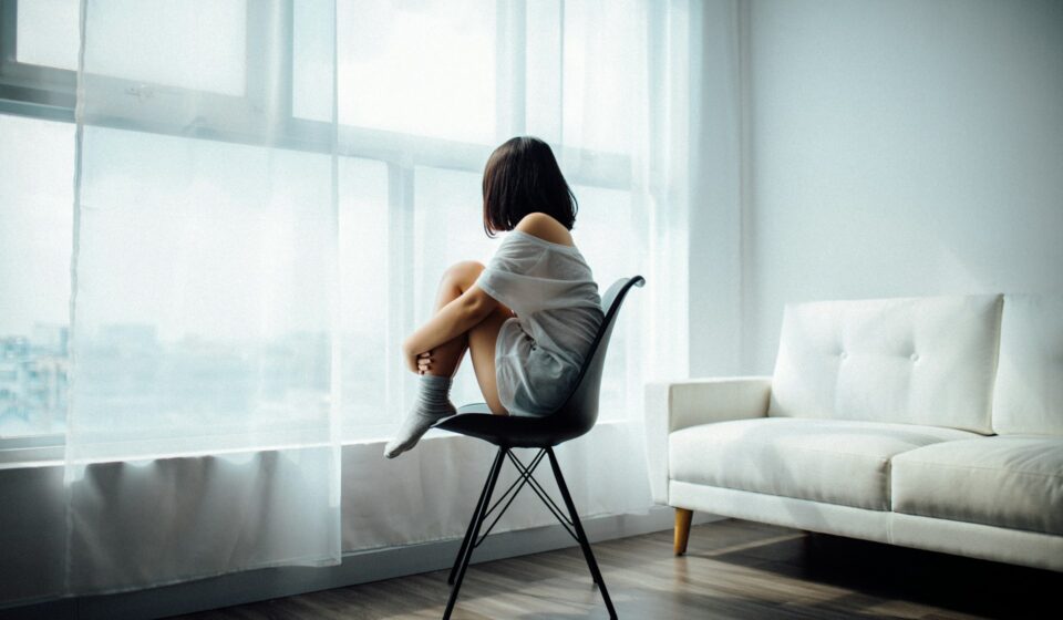 Woman sitting in a chair by a large window, quietly reflecting during a calm moment at home