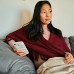 Woman sitting on a couch looking at her phone while reading news or social media updates