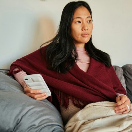 Woman sitting on a couch looking at her phone while reading news or social media updates