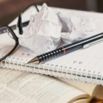 Black-framed eyeglasses resting on a page with blurred text, representing difficulty focusing and mental fog.